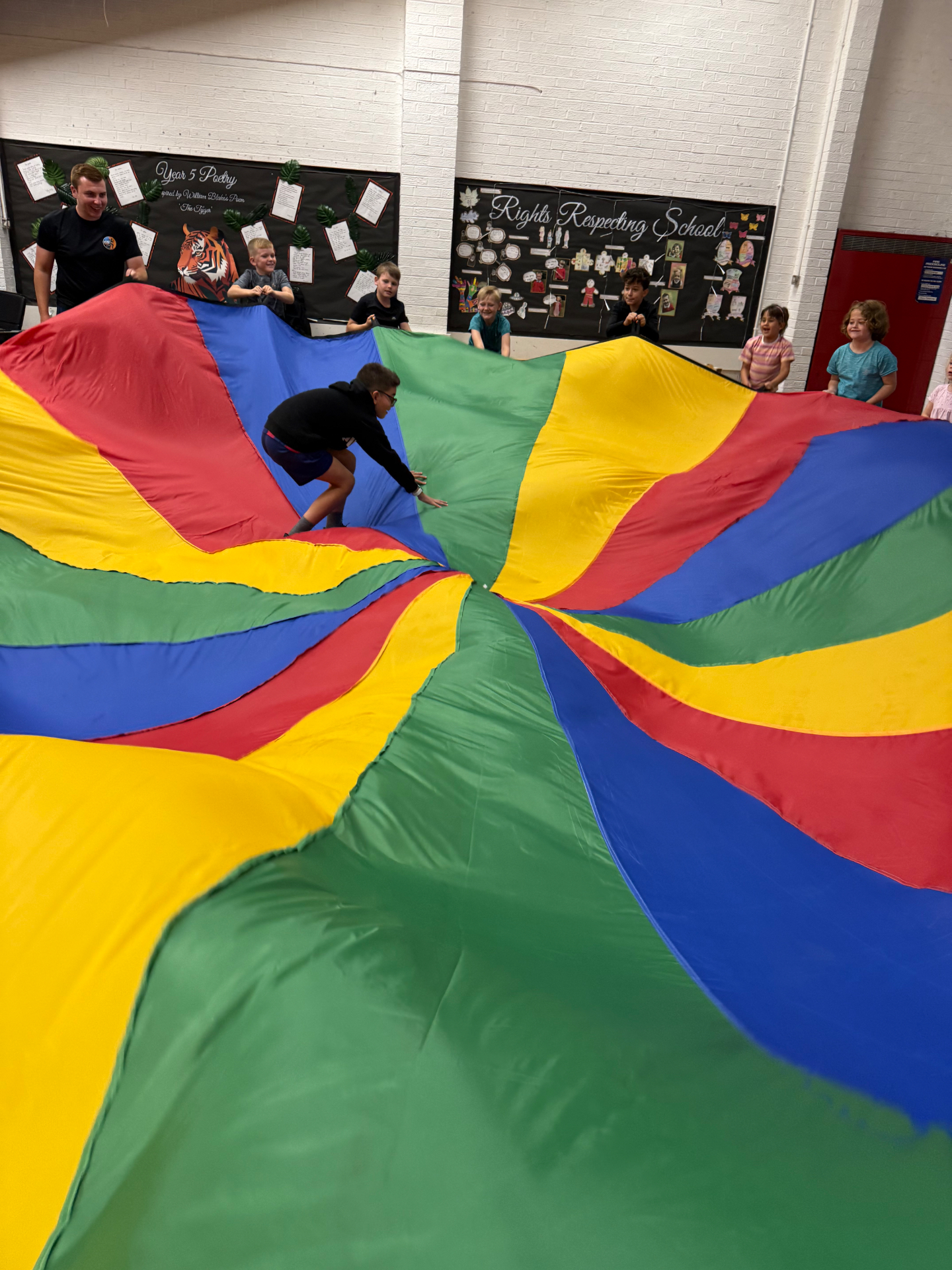 Children playing a parachute game in a school hall